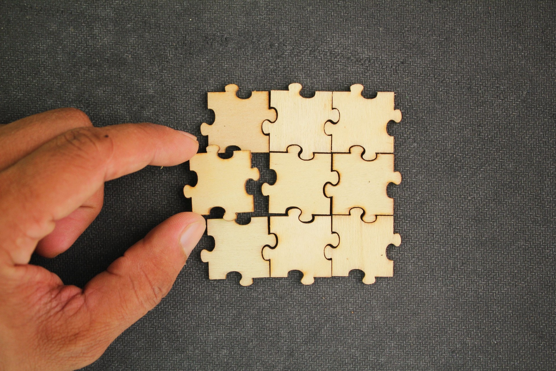 The puzzles are arranged and the hand holds the last puzzle for combination. concept of solution or complete task. teamwork and cooperation concept. Hand to complete last piece wood puzzle.